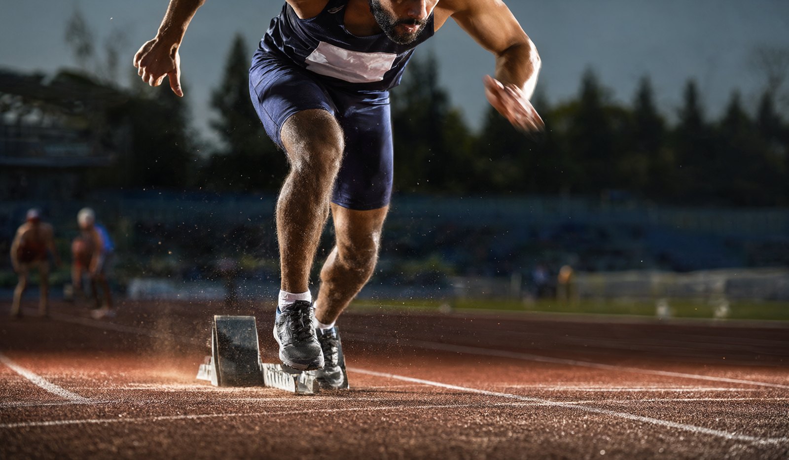 Sports action photograph of a sprinter exploding out of the start blocks with motion blur and late afternoon side light